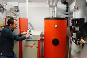  Heizungstechnik mit Pelletskessel 30 kW und Pufferspeicher im Technikraum eines Mehrfamilienhauses. Im Hintergrund die Schläuche eines pneumatischen Entnahmesystems. 