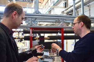  Prof. Dr. Carsten Bäcker (links) und Stefan Brodale schließen eine Armatur an ihr aufgebautes Trinkwasserinstallationsmodell mit Warm- und Kaltwasserleitung an.  