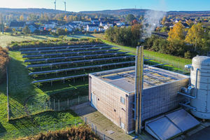  Die Heizzentrale der Ortsgemeinde Ellern liegt am Ortsrand. Rechts neben dem Gebäude sieht man den 105.000 l fassenden Pufferspeicher, im Vordergrund das die Biomassefeuerung unterstützende Solarthermiefeld. 