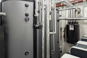  Der Niedertemperaturspeicher wird von den Heizungswärmepumpen geladen und bedient die Heizkreise. Der Speicher dient der eXergiemaschine (schwarzes Gerät an der Wand) zugleich als Quelle. Die eXergiemaschine hebt die Temperatur auf über 65 °C an und speist die Wärme in den Hochtemperaturspeicher, der die Frischwasserstationen versorgt. 